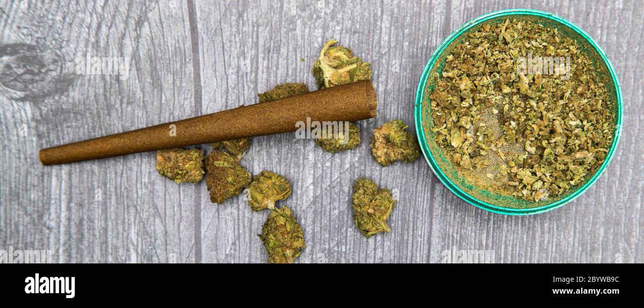 Grandes brotes de marihuana medicinal molida para rodar una articulación. Brotes y molinillo verde sobre mesa de madera. Foto de stock