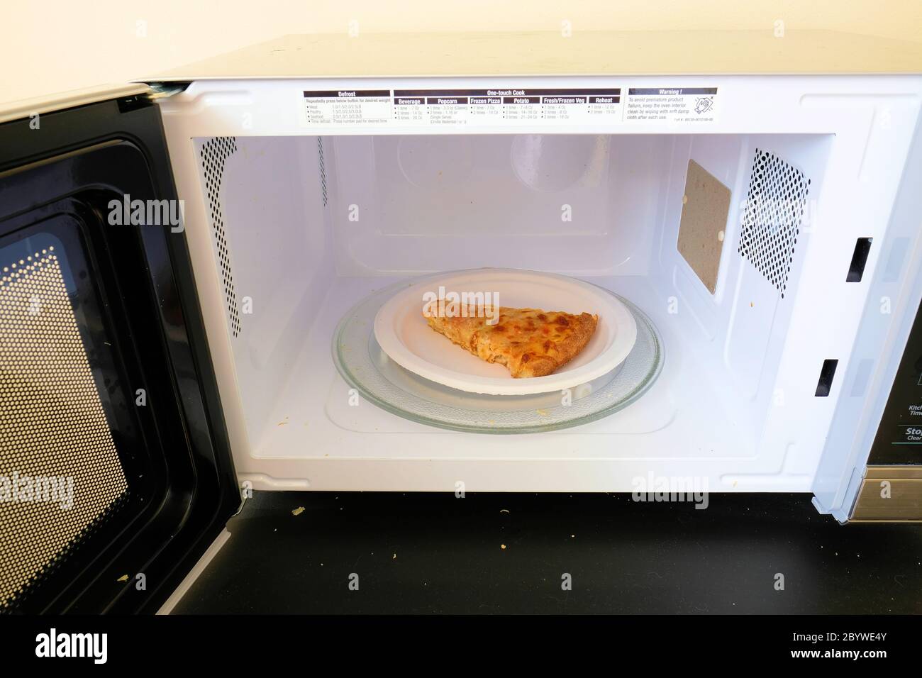 Microondas con la puerta abierta; microondas vacío; trozo de pizza de queso  frío sobrante en un plato de papel listo para hacer microondas Fotografía  de stock - Alamy