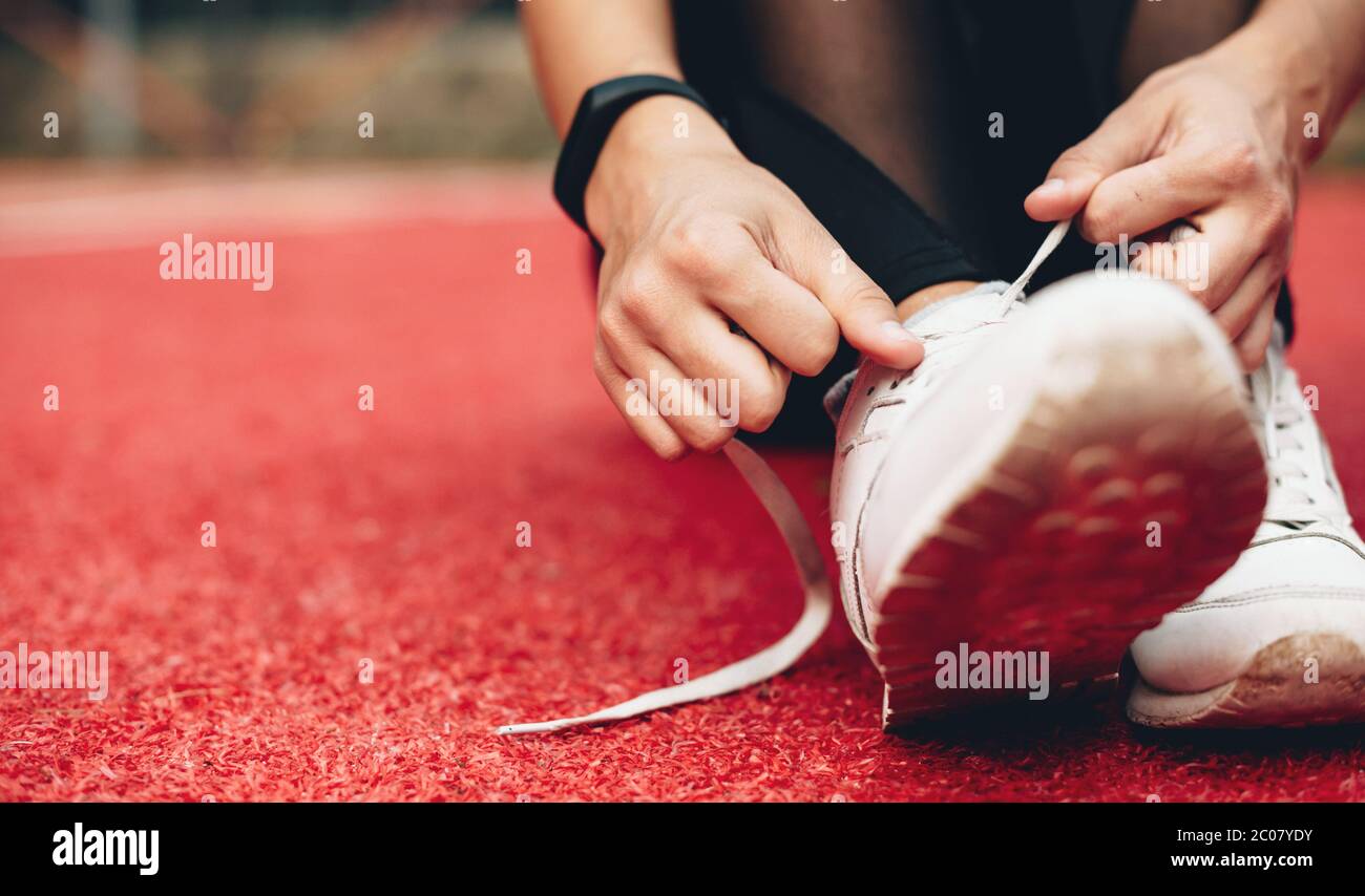 foto de cerca de una chica caucásica preparando sus botas para una sesión de jogging en un estadio deportivo rojo Foto de stock
