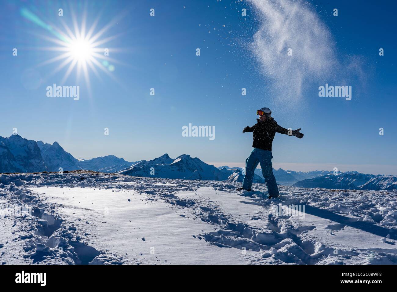 Chica disfrutando de las vigas de sol en invierno mientras lanza nieve en el aire en la cima de la cadena montañosa. Snowboarder a última hora de la tarde en los alpes suizos en el vino Foto de stock