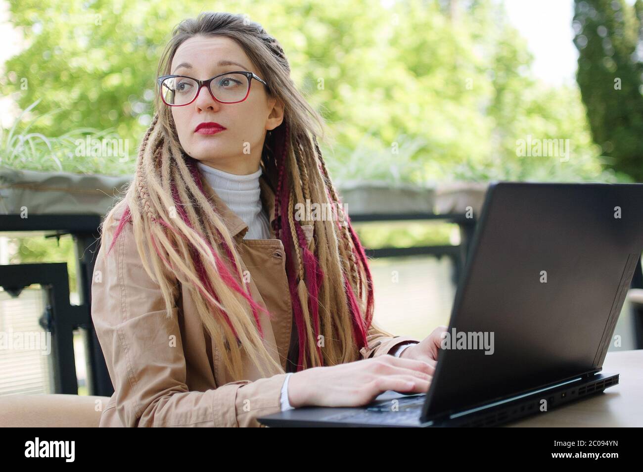 Retrato al aire libre de un estudiante inteligente y con talento con largos dreadlocks se está preparando para los próximos exámenes mientras se sienta en la cafetería al aire libre Foto de stock