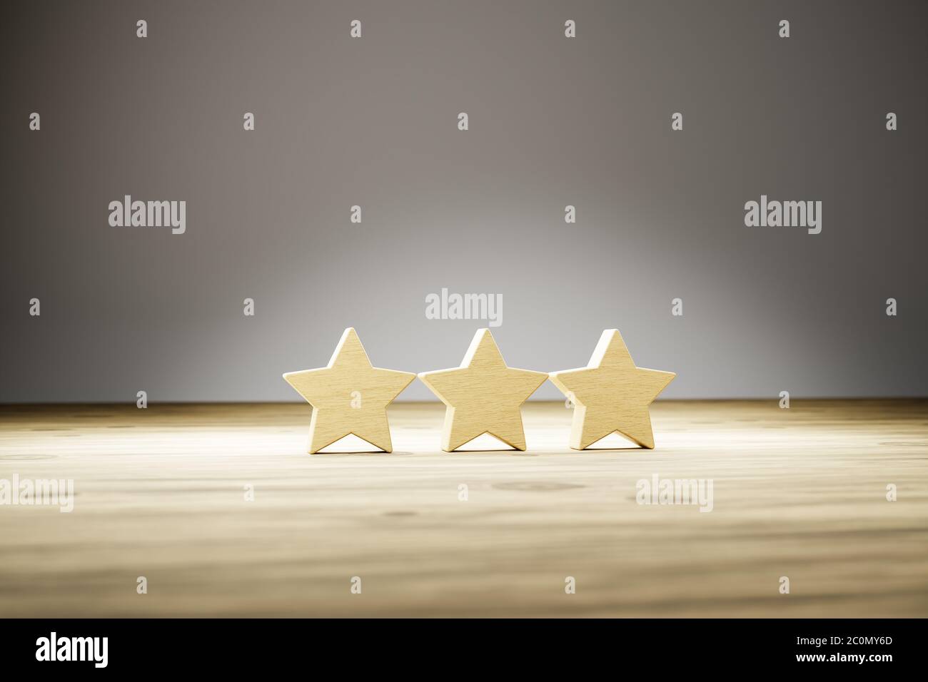 Clasificación de tres estrellas: Tres estrellas de madera en una fila sobre una mesa de madera con fondo gris. Enfoque selectivo. Foto conceptual para la valoración/revisión. Foto de stock