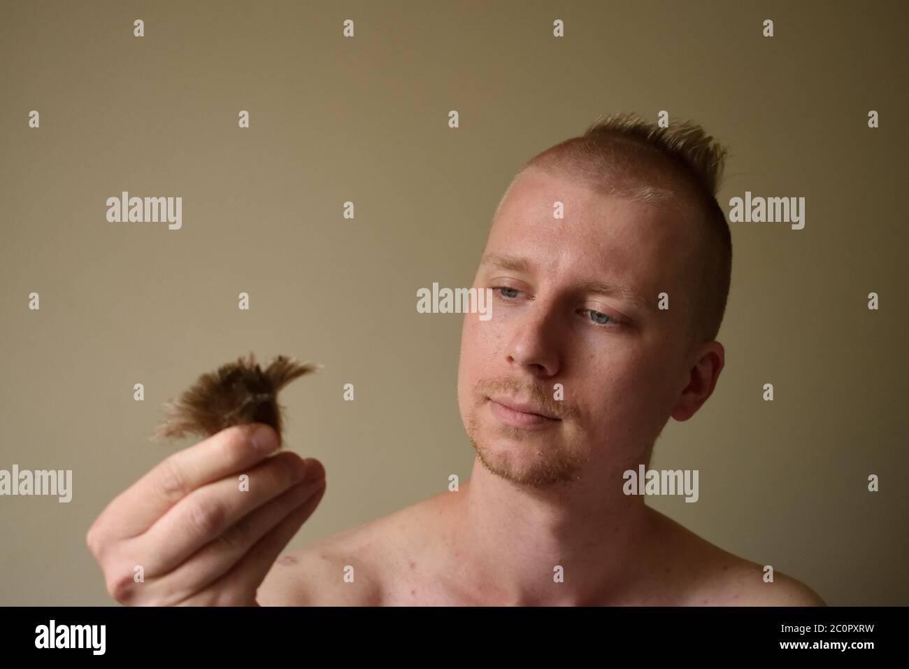 El joven mira lamentablemente a un candado de su pelo después de darse un mal corte de pelo en casa durante el cierre Foto de stock