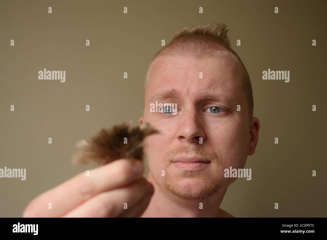 El joven mira lamentablemente a un candado de su pelo después de darse un mal corte de pelo en casa durante el cierre Foto de stock