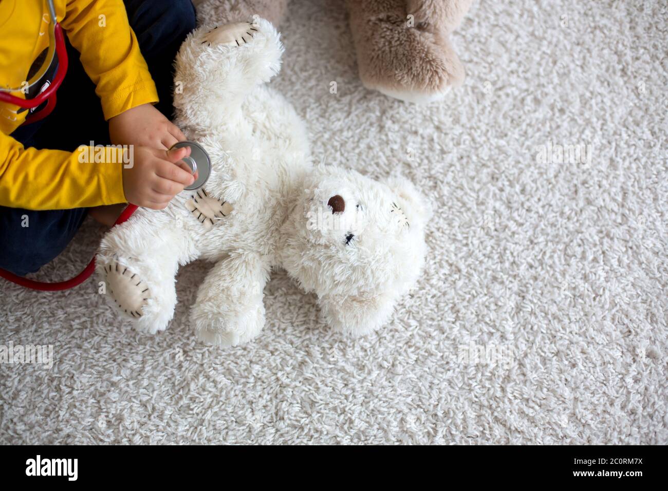 Niño dulce, médico que juega, examinando el juguete de oso de peluche en casa, fondo aislado Foto de stock