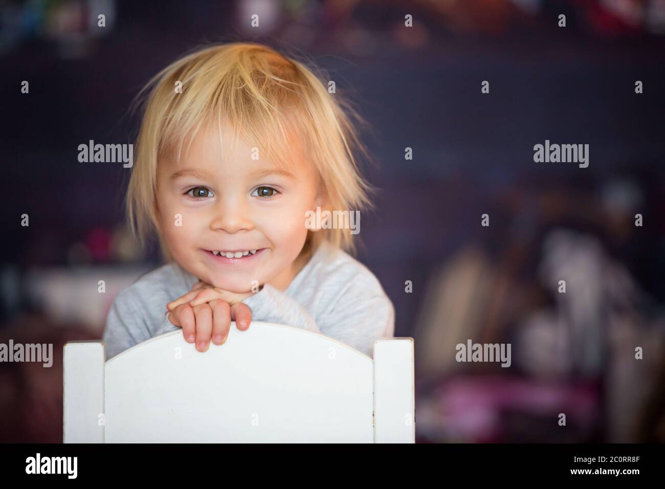 Hermoso niño rubio, sentado en una silla, jugando con juguetes en una sala de juegos Foto de stock