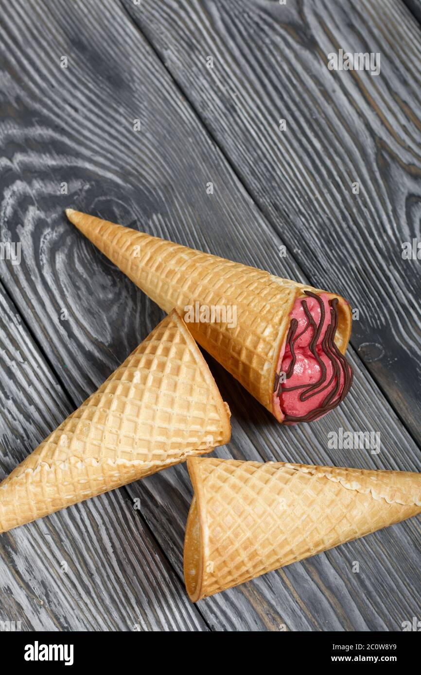 Helado de fresa en un cono de waffle. Adornada con chocolate. Cerca hay  conos vacíos de waffles sin helado. En tablas de pino pintadas en negro y  Fotografía de stock - Alamy