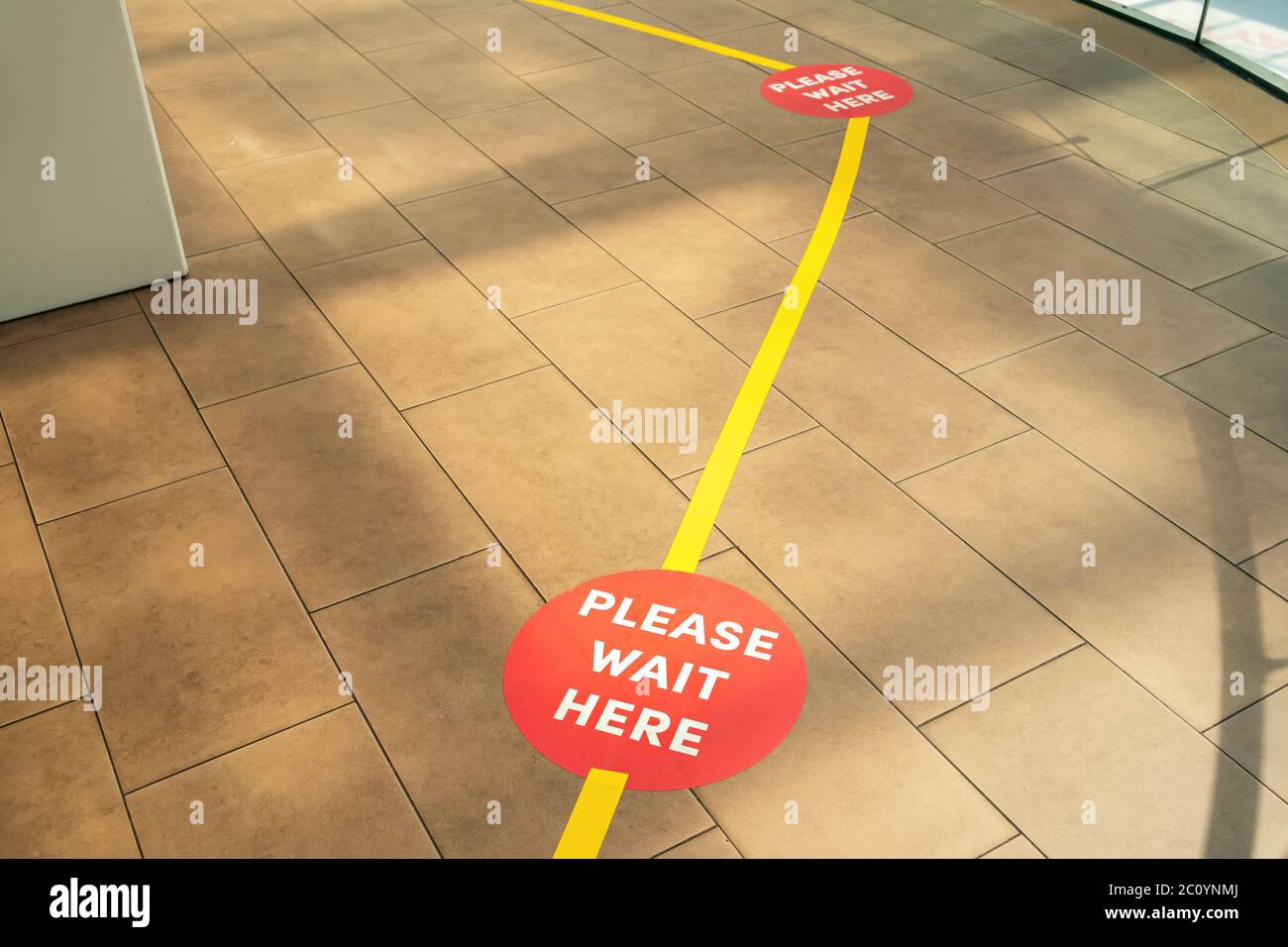 Línea de Compras a distancia Social. Asegure las líneas de cinta amarilla en el suelo para esperar en la tienda. Espere aquí, por favor. Foto de stock