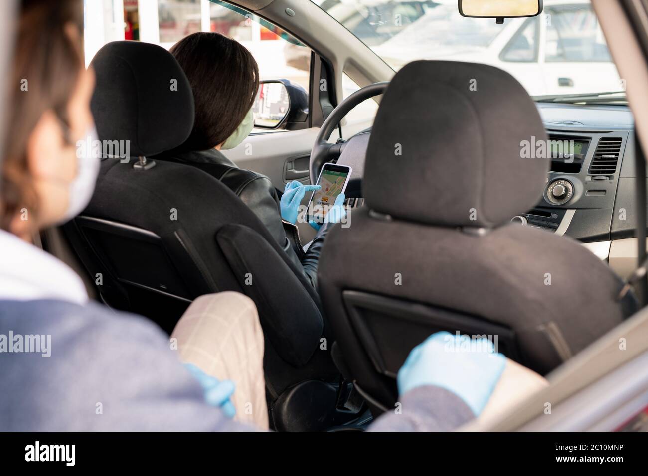 Vista sobre el hombro del taxista en máscara utilizando la aplicación para smartphone mientras analiza la ruta al destino del cliente Foto de stock