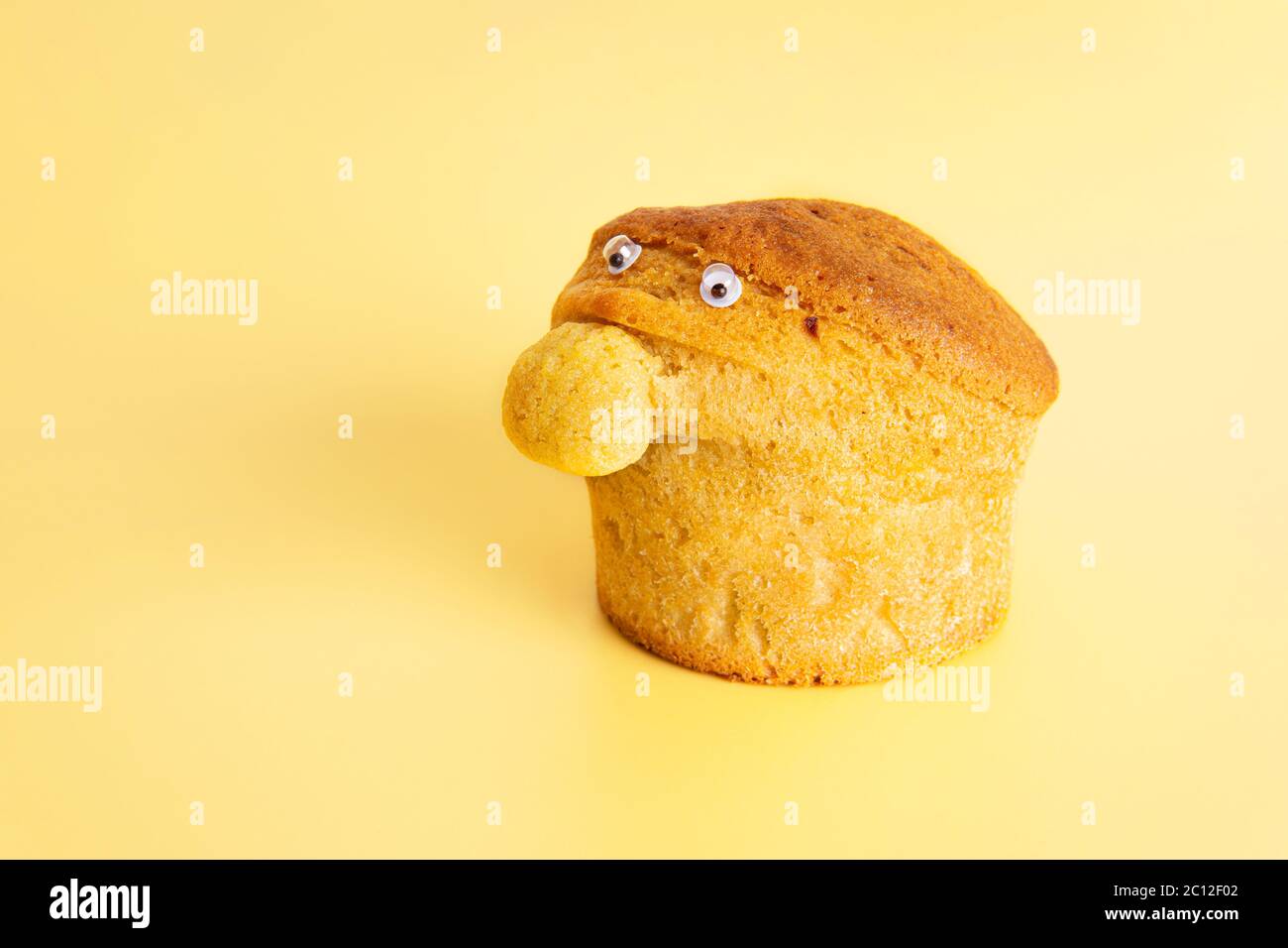 Muffin casera con una nariz grande y ojos pequeños sobre un fondo amarillo. Carácter divertido de la comida. Foto de stock
