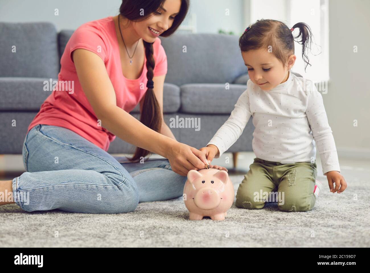 La joven madre y su hija ponen monedas en el banco de palomas en casa. Padres que dan educación financiera a su hijo Foto de stock