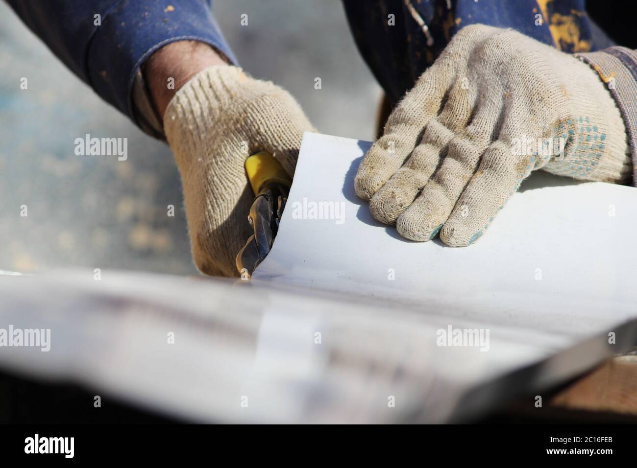 El trabajador hace el corte de ventanas en el edificio restaurado de la ciudad, corta la chapa metálica de la pendiente con tijeras. Foto de stock
