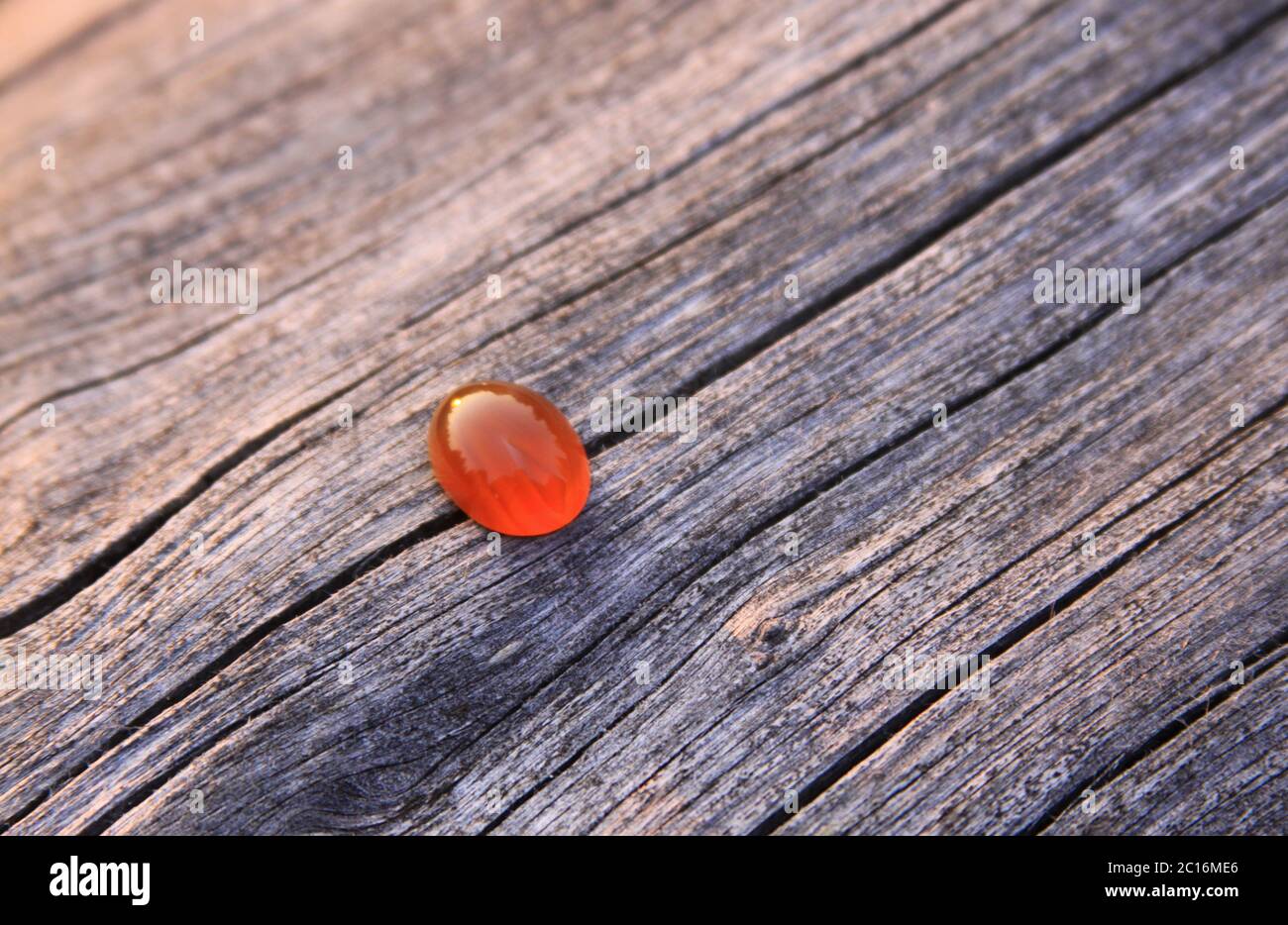 Una piedra preciosa aislada de color rojo de calcedonia naranja agate sobre fondo de madera que brilla en la luz del sol. Las gemas de calcedonia vienen en una variedad de colores diferentes Foto de stock