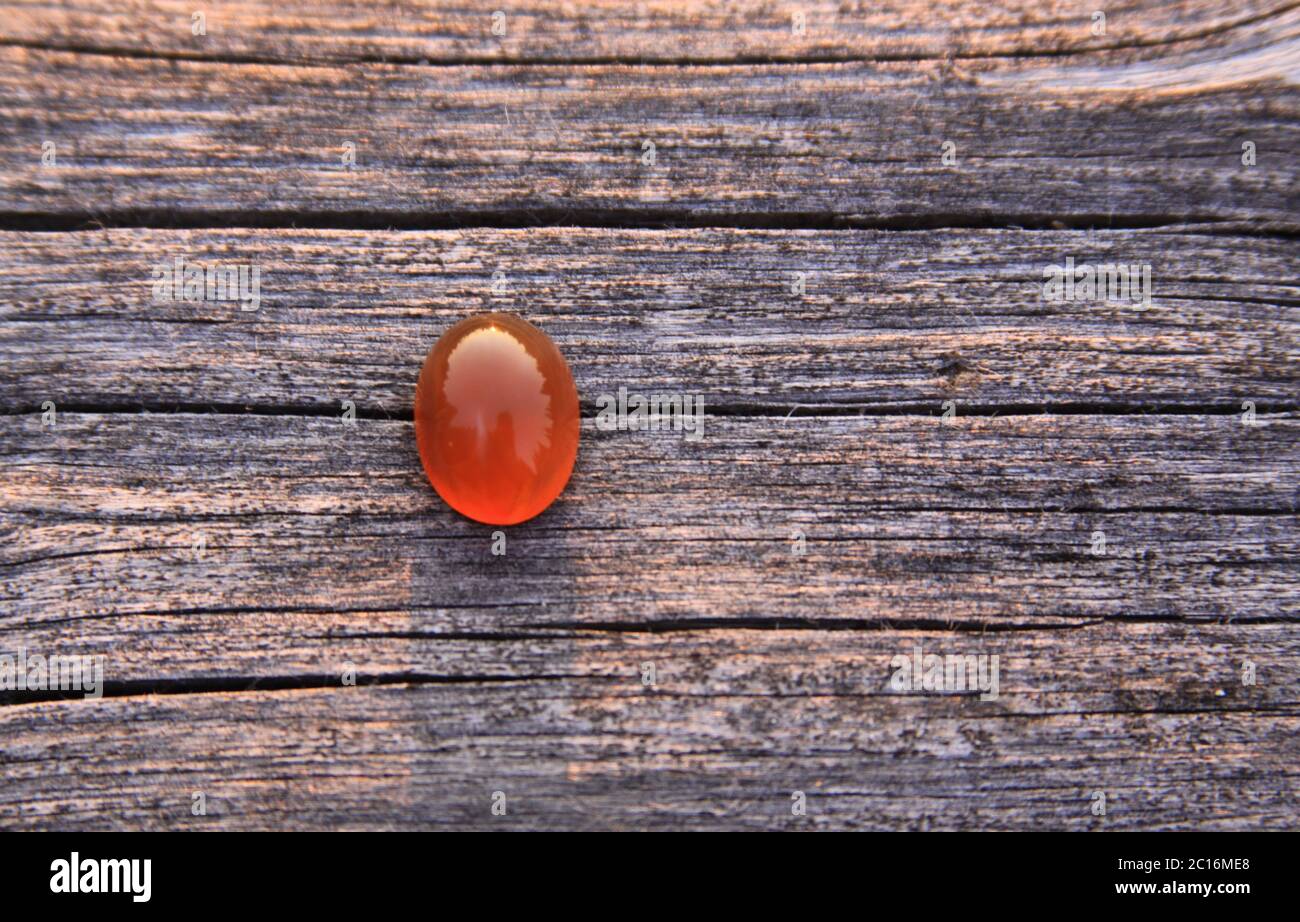 Una piedra preciosa aislada de color rojo de calcedonia naranja agate sobre fondo de madera que brilla en la luz del sol. Las gemas de calcedonia vienen en una variedad de colores diferentes Foto de stock