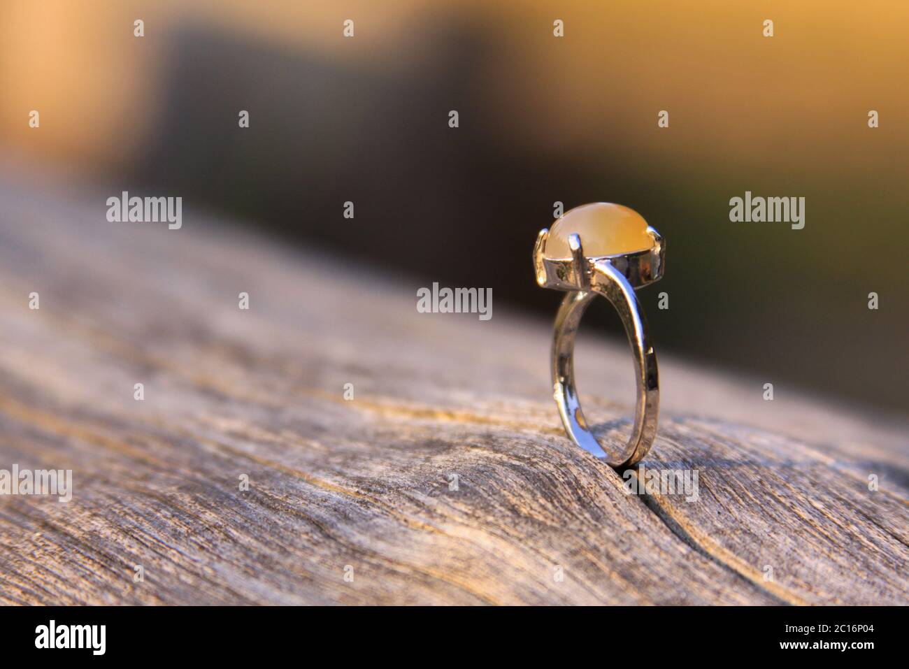 Anillo de compromiso con crema de color amarillo naranja calcedonia agate gemstone sobre madera. Las gemas de calcedonia vienen en una variedad de colores diferentes y son normalmente pol Foto de stock