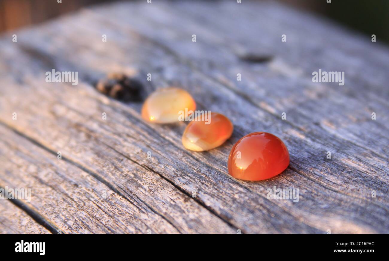 Tres calcedonia coloreada agate piedras preciosas sobre fondo de madera que brilla en la luz del sol. Las gemas de calcedonia vienen en una variedad de colores diferentes y son u Foto de stock