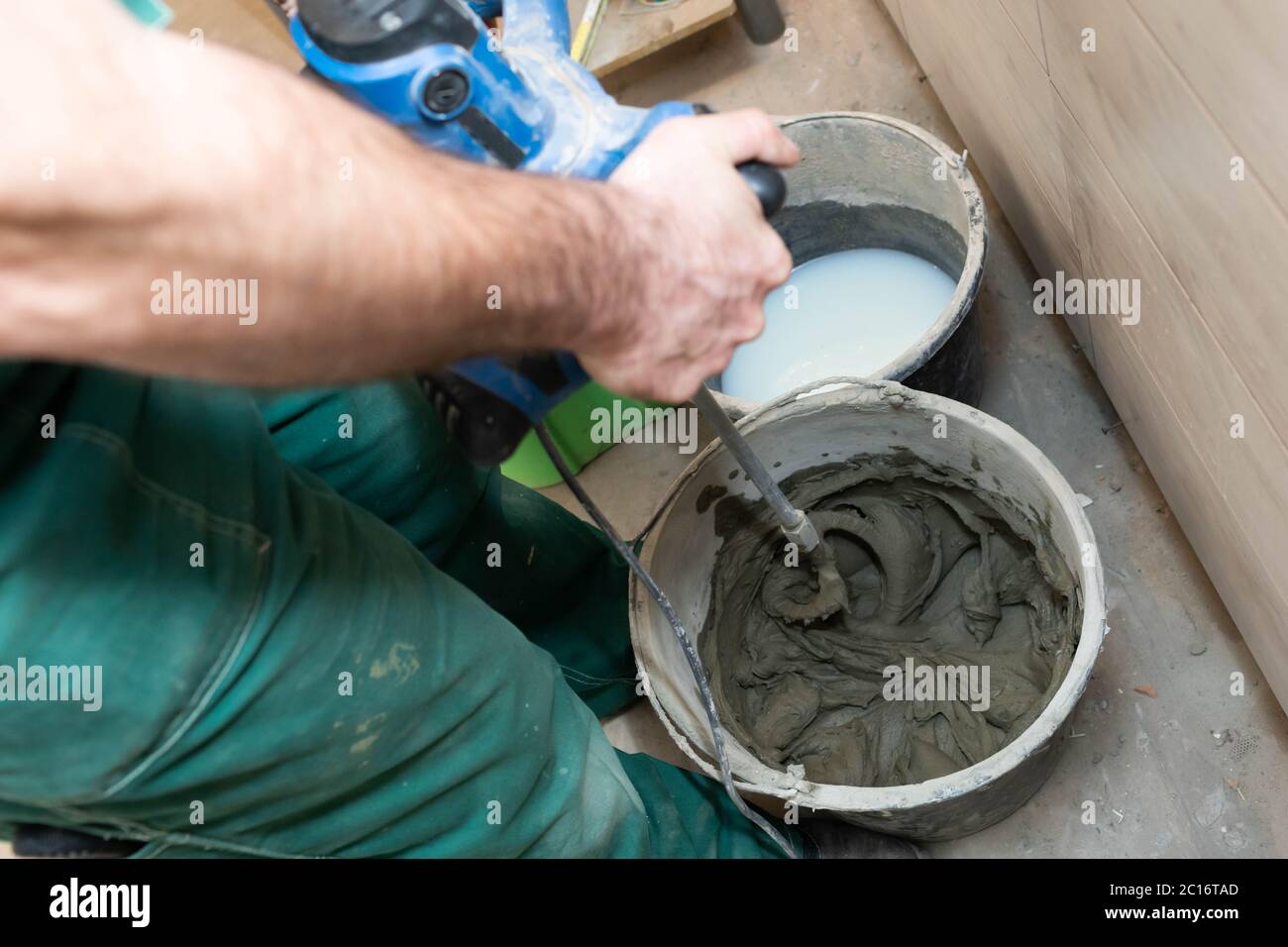 Trabajador mezclando mortero seco con batidora de mano en balde en