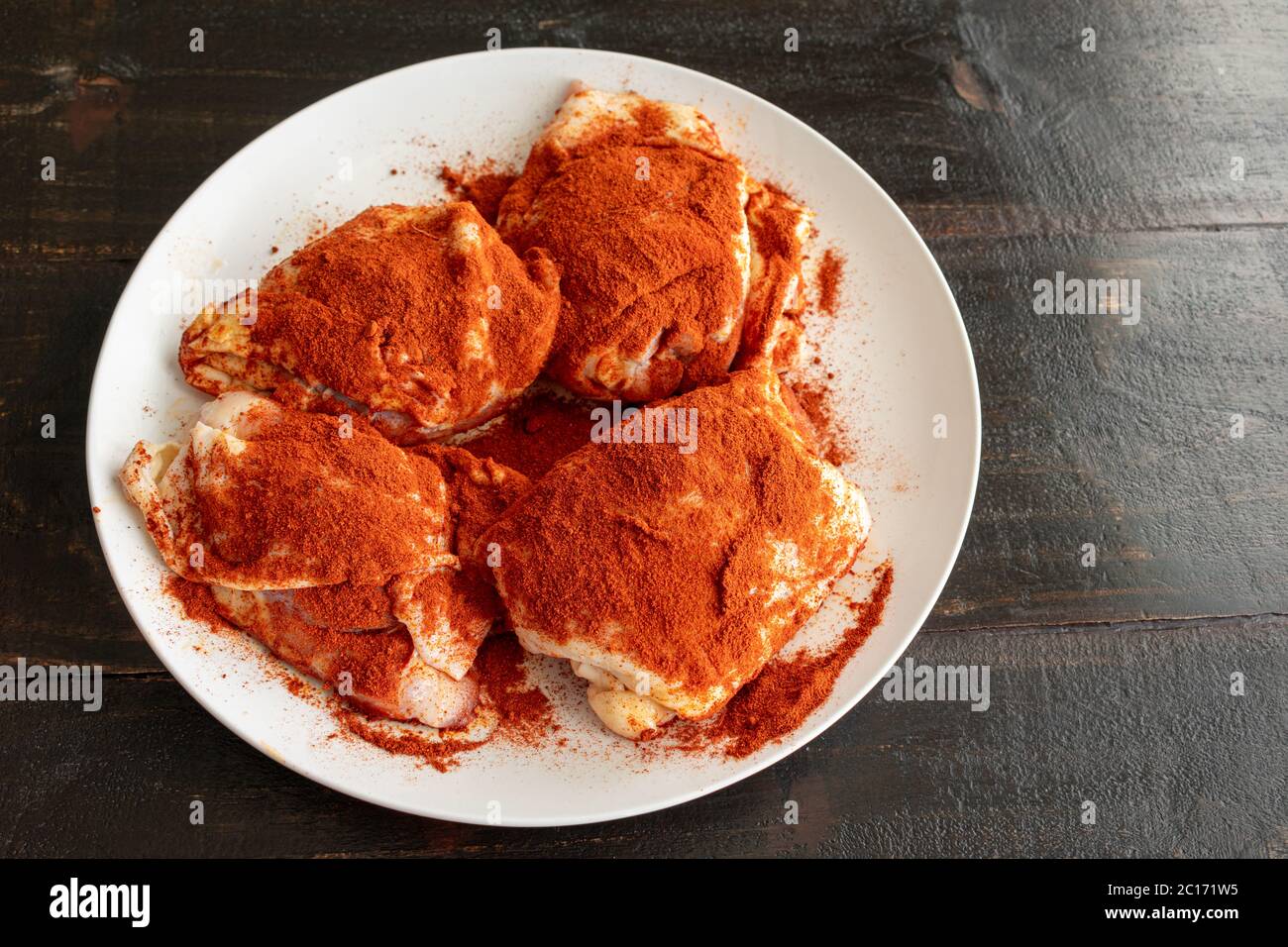 Muslos de pollo condimentados con Paprika para pollo Paprikash: Muslos de pollo crudos rociados con pimenton y pimenton (pimentón ahumado) Foto de stock