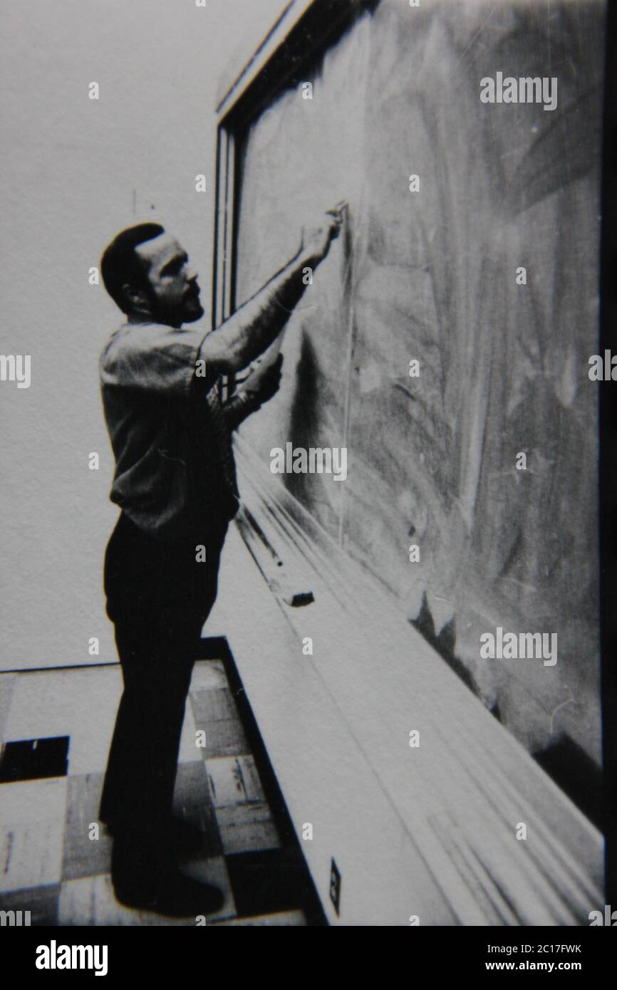 Fotografía extrema de los años 70 de la vendimia fina en blanco y negro de un profesor parado en la pizarra y escribiendo en ella. Foto de stock