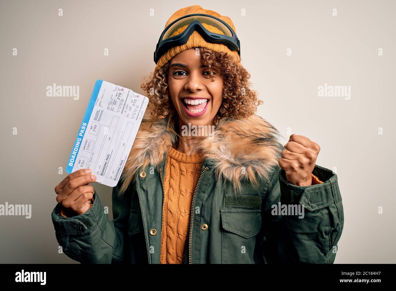 Joven turista afroamericana con gafas de esquí sosteniendo billetes de avión gritando orgulloso y celebrando la victoria y el éxito muy Foto de stock