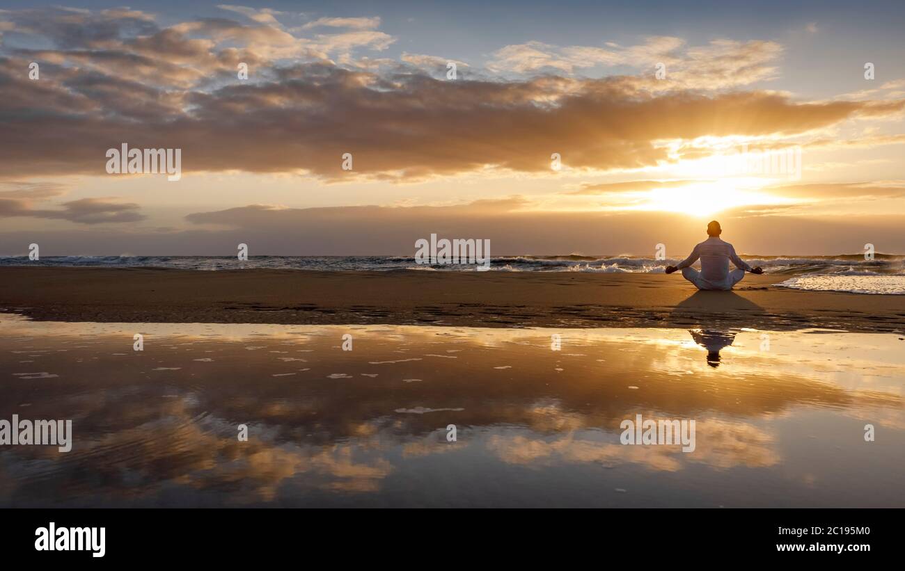 yoga meditación silueta lotus amanecer playa, atención, bienestar y concepto de bienestar, agua reflexión del hombre en yoga loto pose sentado solo Foto de stock