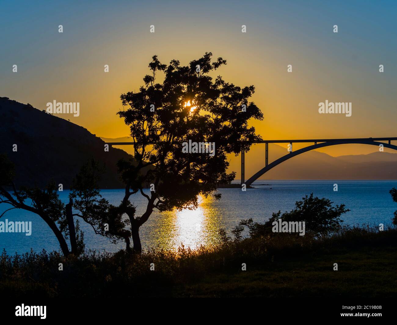 Puesta de sol paisaje puente continental a la isla Krk Croacia ver vista a través de árbol dominante Foto de stock