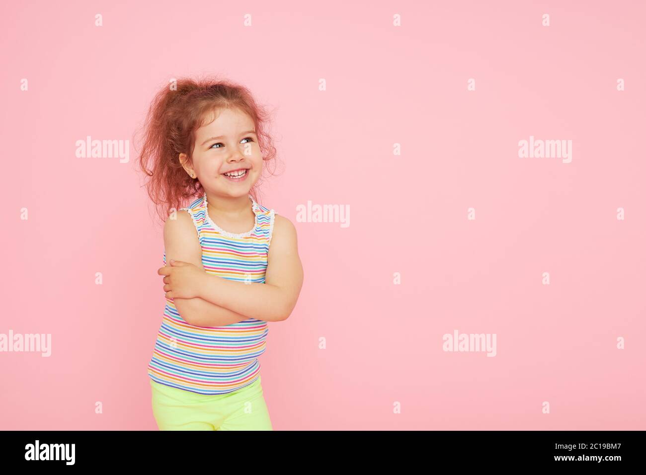 Retrato de una niña pequeña y linda con una sonrisa blanca como la nieve y dientes sanos sobre fondo rosa. Mirando la cámara y riendo. Odontología para c Foto de stock