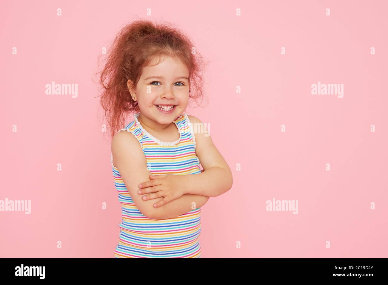 Retrato de una niña pequeña y linda con una sonrisa blanca como la nieve y dientes sanos sobre fondo rosa. Mirando la cámara y riendo. Odontología para c Foto de stock
