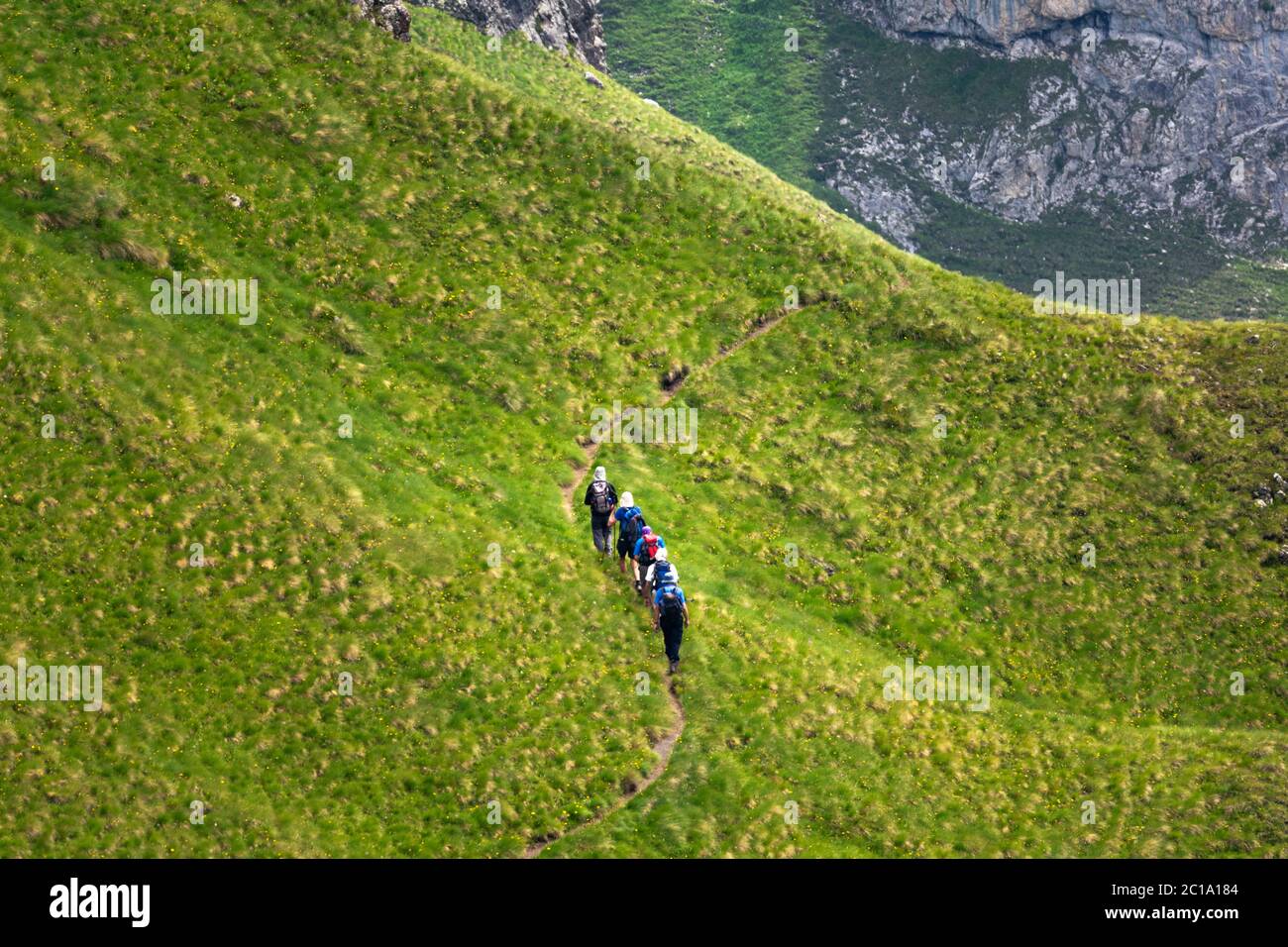 Foto aérea de una caravana de gente o grupo de amigos caminando en una ladera en un camino estrecho. Excursionistas y exploradores caminando en la montaña. Foto de stock