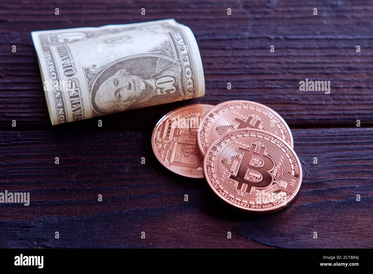 Billetes de dólar y Bitcoins en una mesa de madera oscura Foto de stock