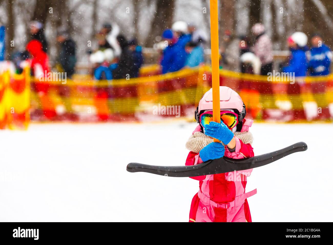 Niña gafas protectoras y un casco en vacaciones de invierno al aire libre fijación de esquís detrás buscando cámara sonriendo emocionada cerca fondo borroso Foto de stock