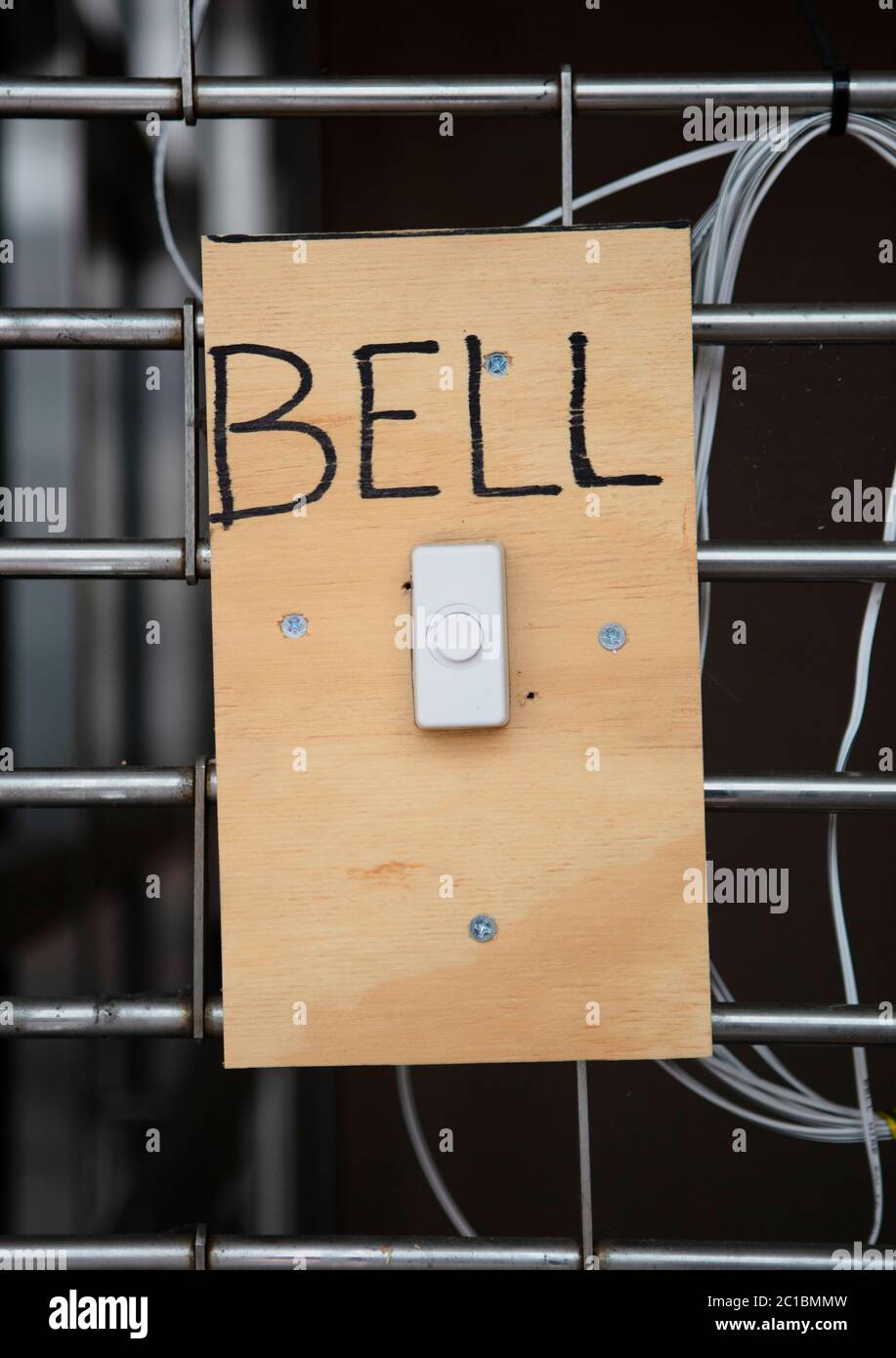 Una campana blanca de la puerta en un pedazo de madera con tornillos con la palabra Bell Foto de stock