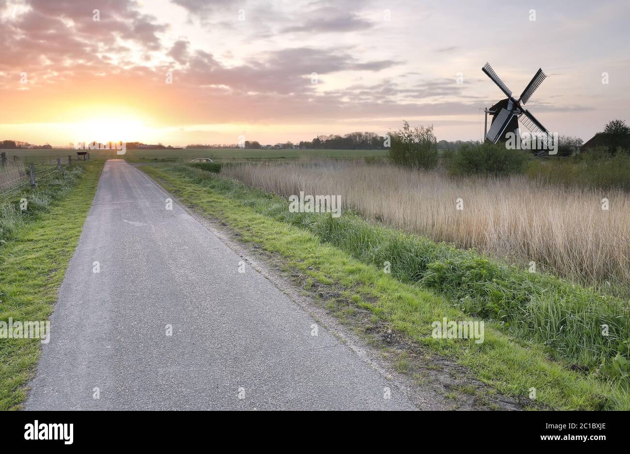 amanecer sobre carretera rural y molino de viento Foto de stock
