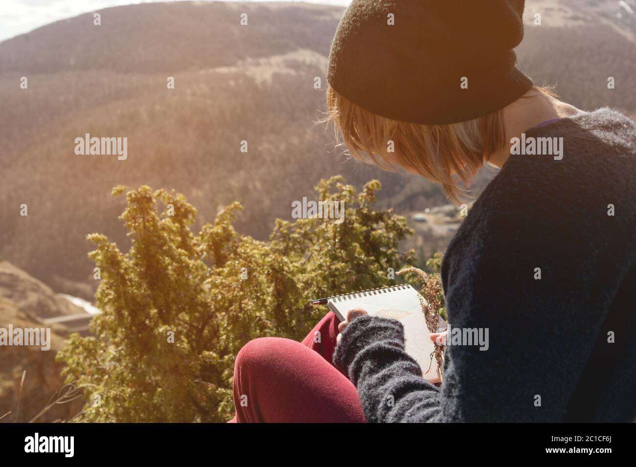 Retrato de una hipo chica con gafas de sol y un sombrero sentado en una roca al aire libre en las montañas contra un cielo azul. Independiente Foto de stock
