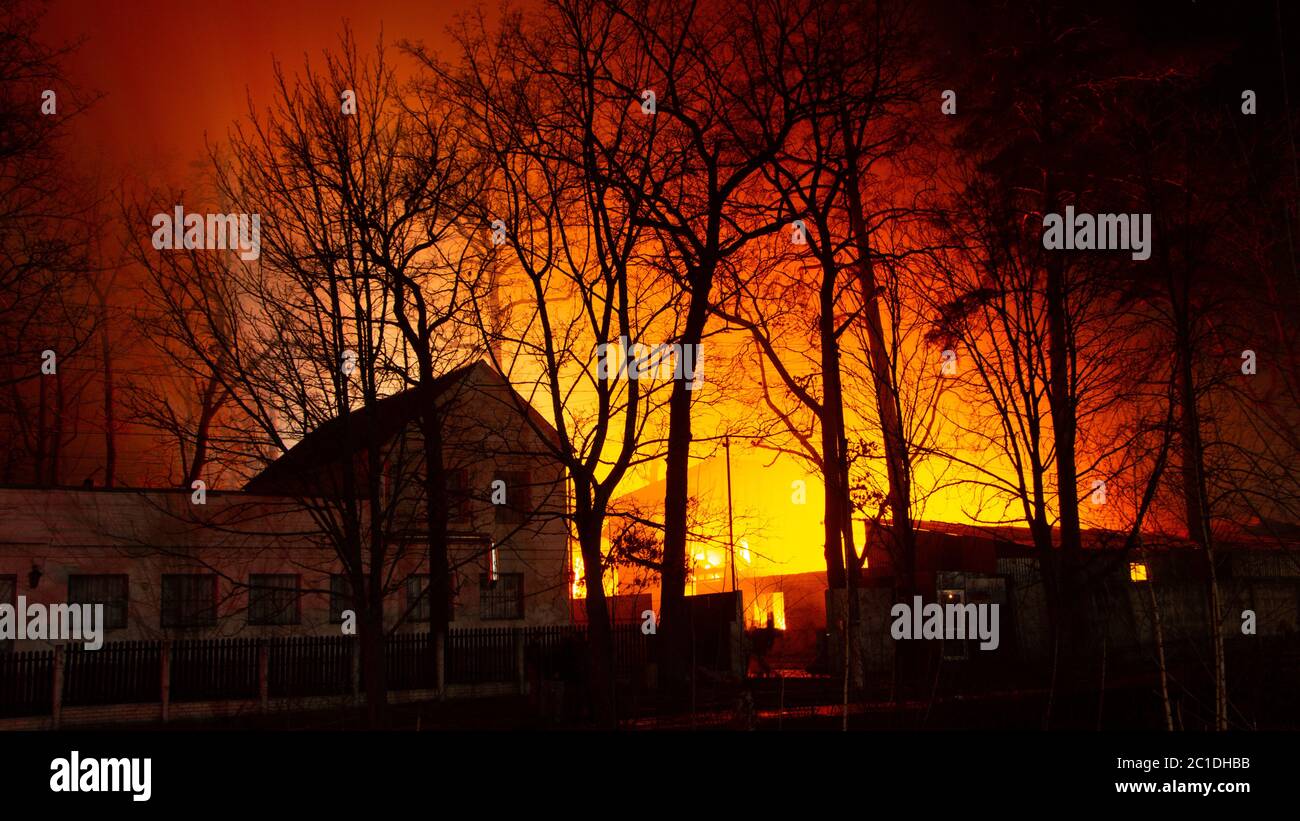 Incendio en el edificio de la fábrica por la noche. Los bomberos intentan apagar el fuego Foto de stock