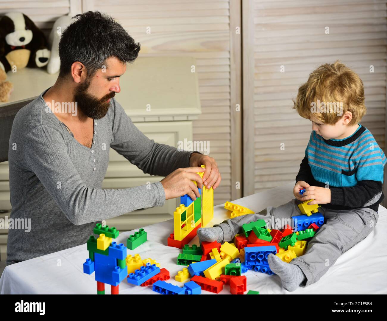 Papá y kid construir casa bloques de plástico. Concepto de la infancia y juegos educativos. Hombre y niño jugar fondo de madera. Padre e hijo con caras ocupado crear coloridos