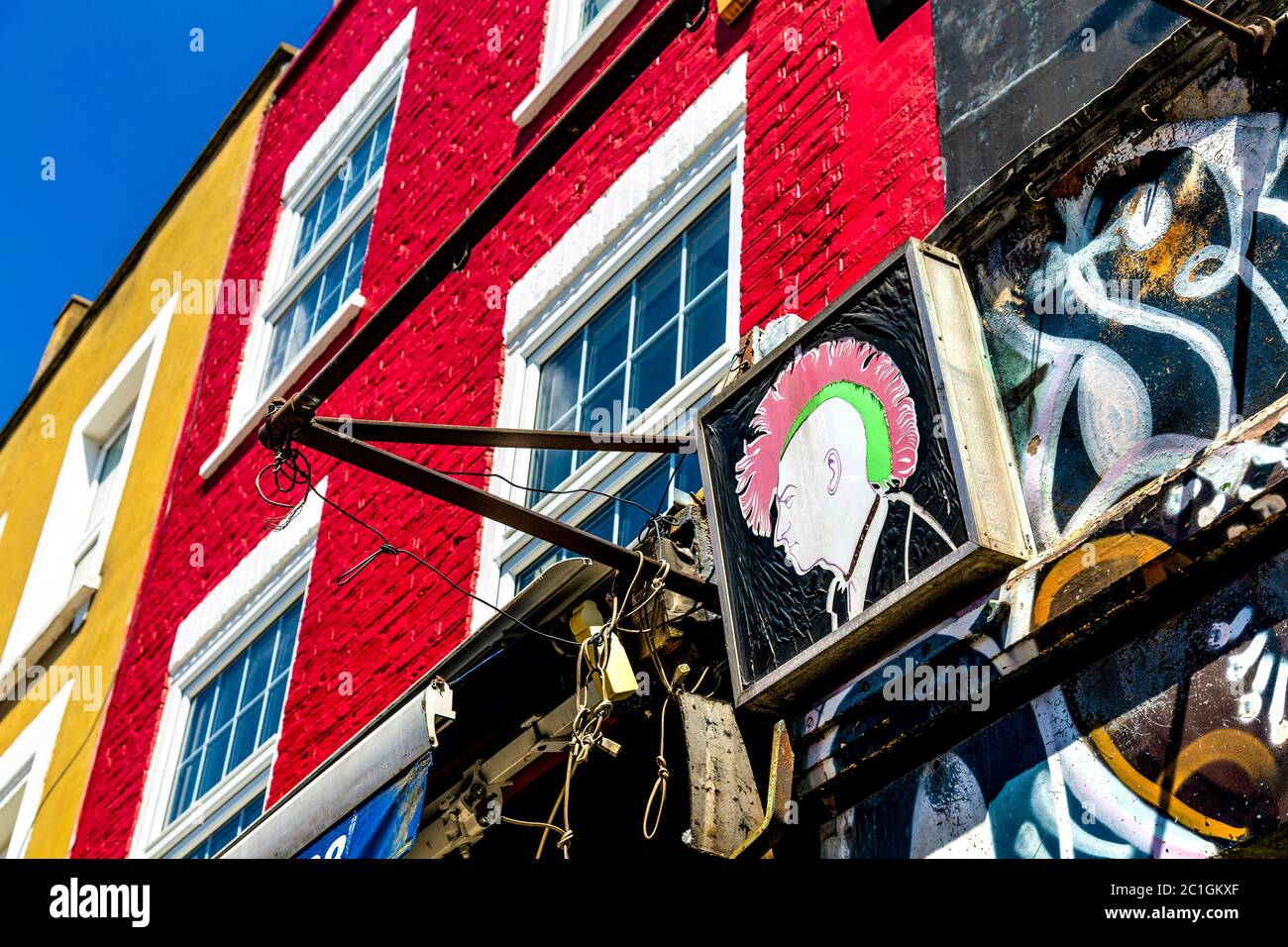 Un cartel con un punk que escudriña un halcón y fachadas de colores de casas a lo largo de Camden High Street, Londres, Reino Unido Foto de stock