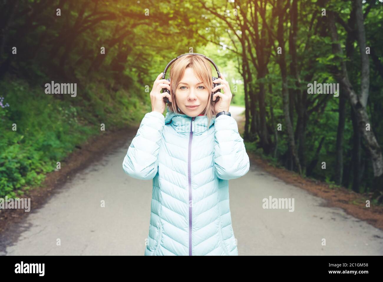 Retrato de una hermosa mujer joven sosteniendo auriculares escuchando música al aire libre en el bosque. Música alegre Foto de stock