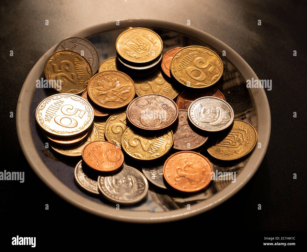 Pequeñas monedas de dinero en un plato sobre fondo negro. Foto de stock