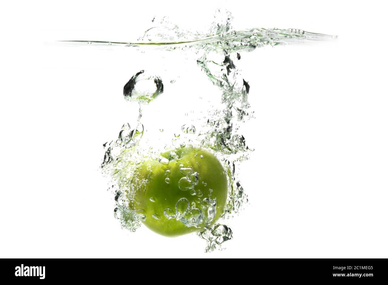una manzana verde cayendo en el agua sobre un fondo blanco con salpicaduras, gotas y burbujas. Foto de stock
