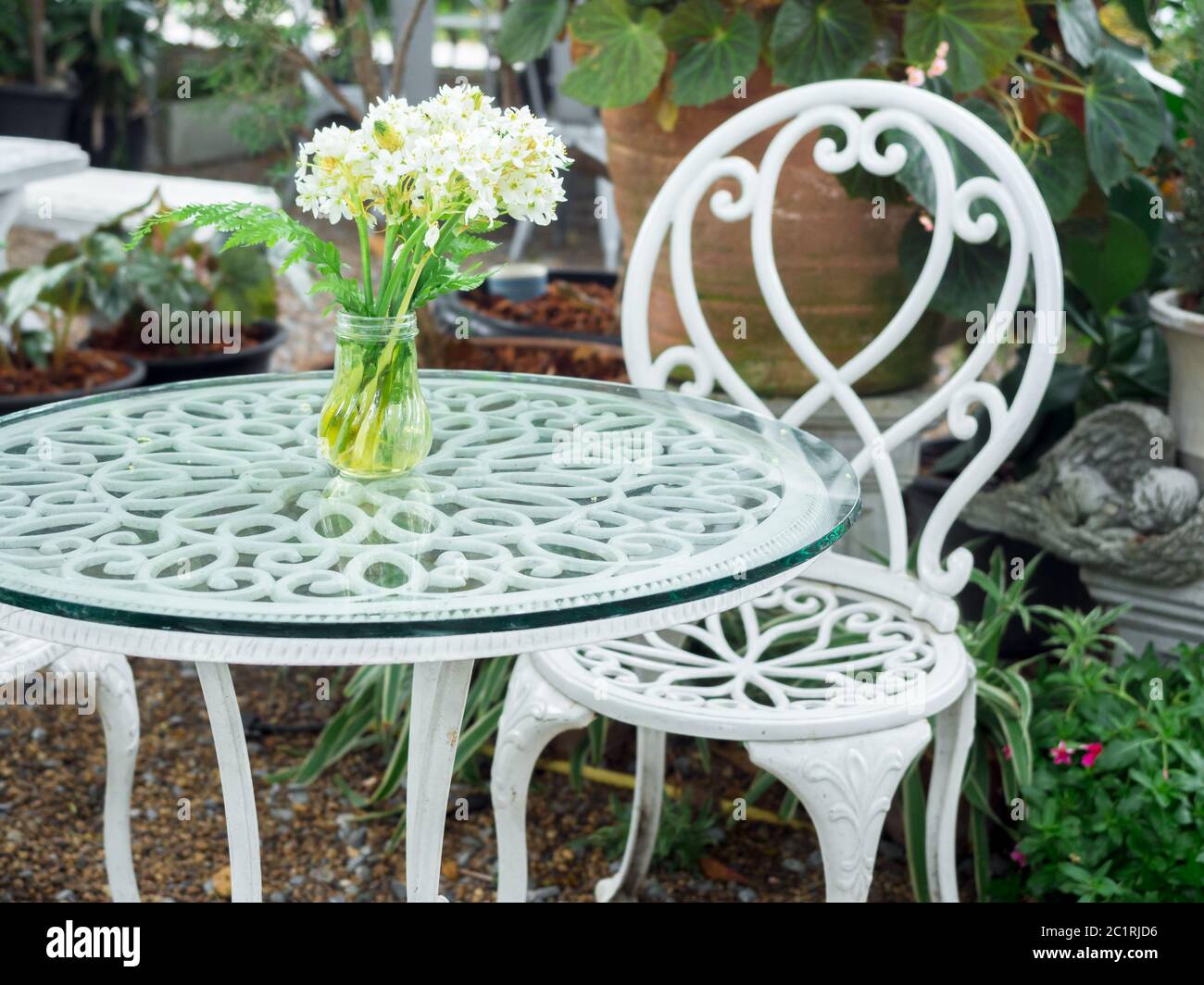 Mesa blanca de hierro forjado con flor blanca en jarrón sobre cristal y  silla estilo vintage en el jardín Fotografía de stock - Alamy