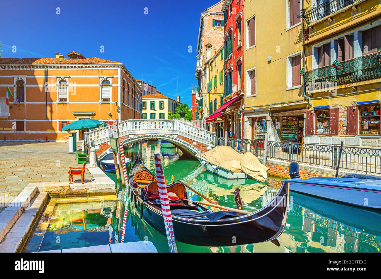 Paisaje urbano de Venecia con góndola y lanchas a motor amarradas en el estrecho canal de agua Río dei Frari, edificios coloridos y puente de piedra, región del Véneto, norte de Italia, fondo azul cielo en el día de verano Foto de stock