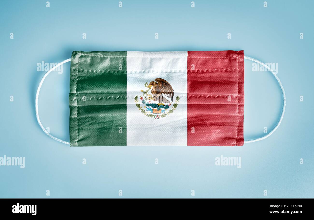 Covid-19 concepto de protección contra el Coronavirus: Mascarilla facial desechable médica con bandera de México sobre fondo azul. Concepto de distanciamiento social. Foto de stock