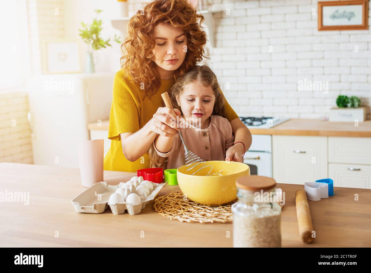 La madre y la hija preparan un pastel juntos en la cocina Foto de stock