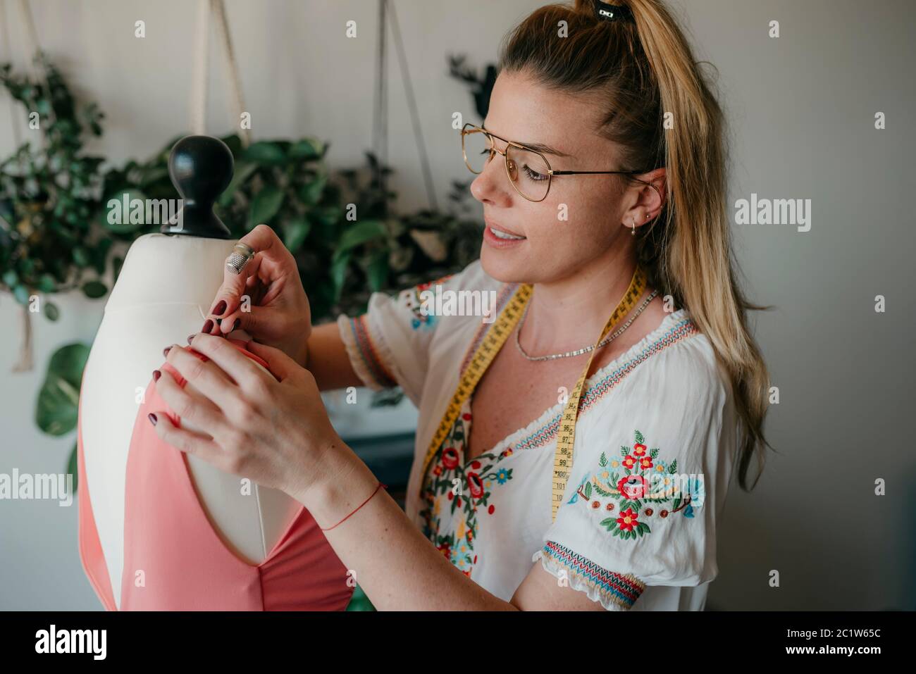 Mujer joven diseñadora de moda medida mannequin, costureras de sujeción de cinta trabajando con maniquí en casa acogedor o tienda de sastre, costura y costura Foto de stock