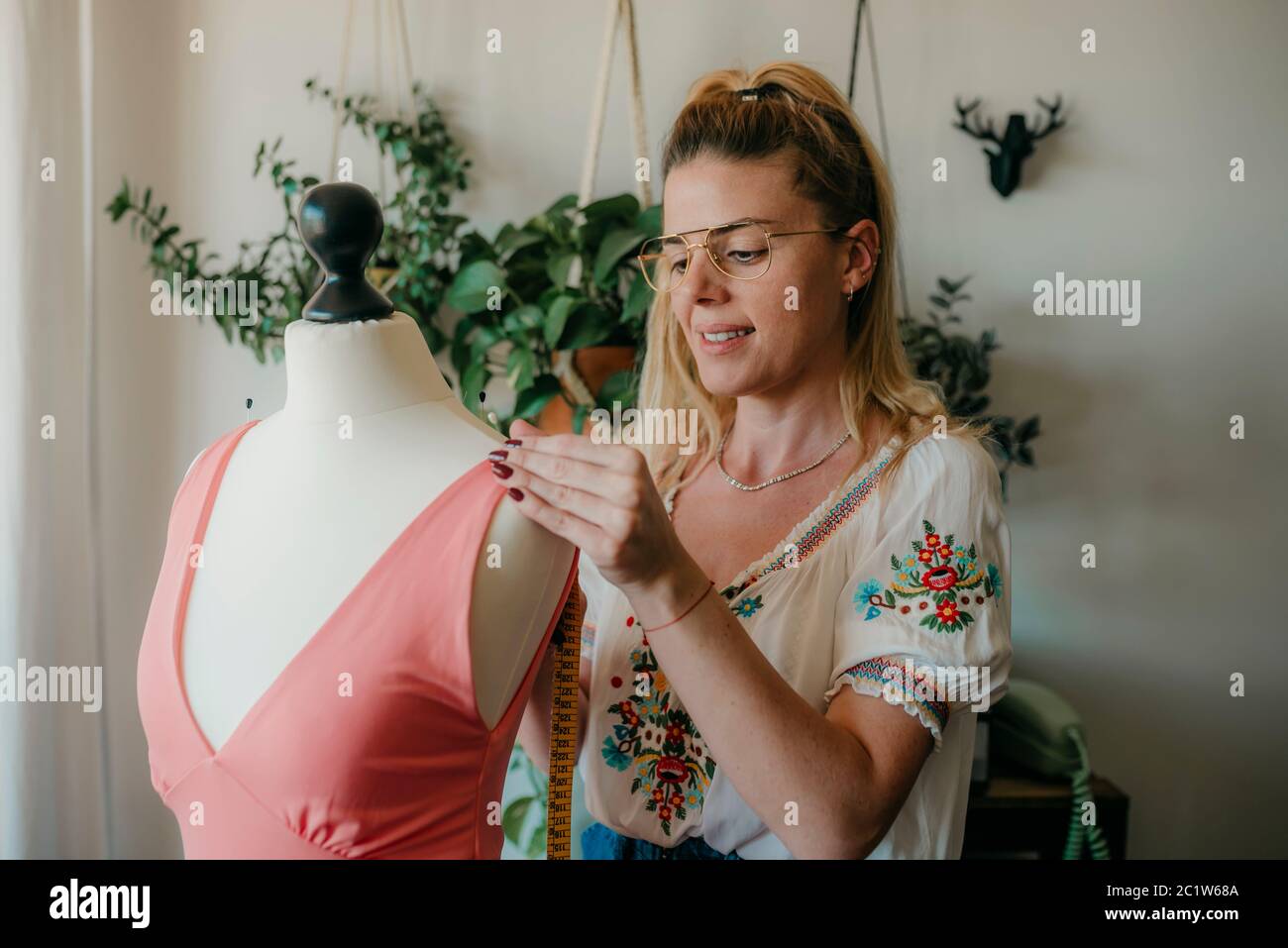 Mujer joven diseñadora de moda medida mannequin, costureras de sujeción de cinta trabajando con maniquí en casa acogedor o tienda de sastre, costura y costura Foto de stock