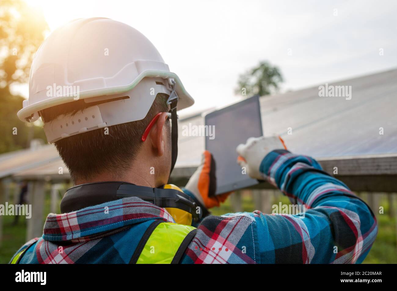 Ingeniero inspeccionando o reparando las celdas solares en una granja solar, comprobando el voltaje con una tableta. Foto de stock