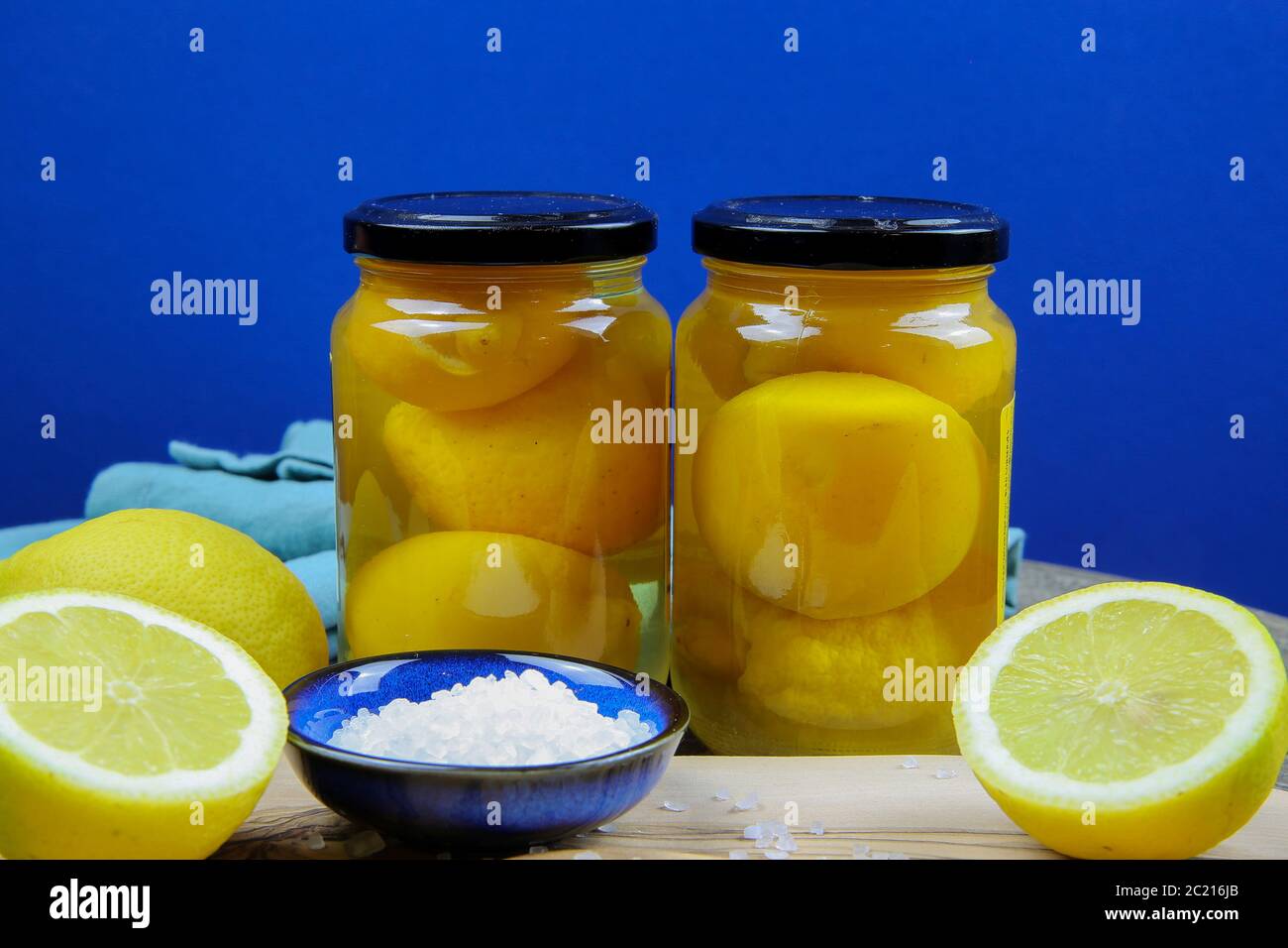 Preparación de limones de sal en conserva marroquí: Primer plano de cítricos amarillos aislados en rodajas, cuenco azul y cuchara de madera con sa de mar gruesa Foto de stock