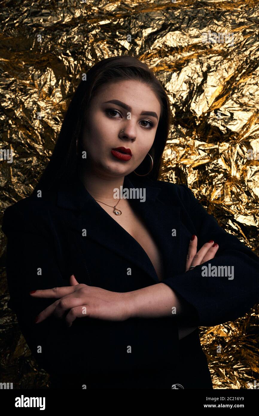 Chica chubby con estilo posando en una chaqueta negra sobre un fondo dorado  Fotografía de stock - Alamy