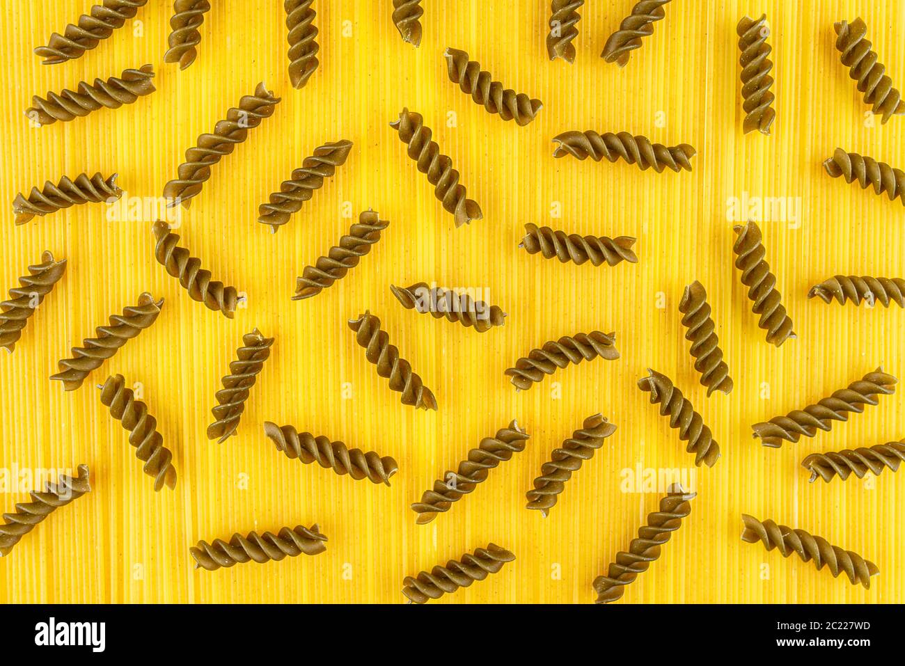 Una pasta espiral verde oscuro sobre un fondo amarillo hecho de pasta espaguetis amarilla larga, vista superior. Foto de stock